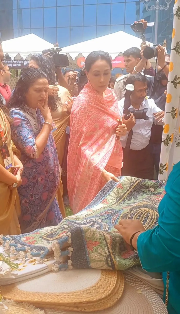 A guest in a coral dupatta and others gathered around a patterned rug at the Dakchi stall, with cameras behind