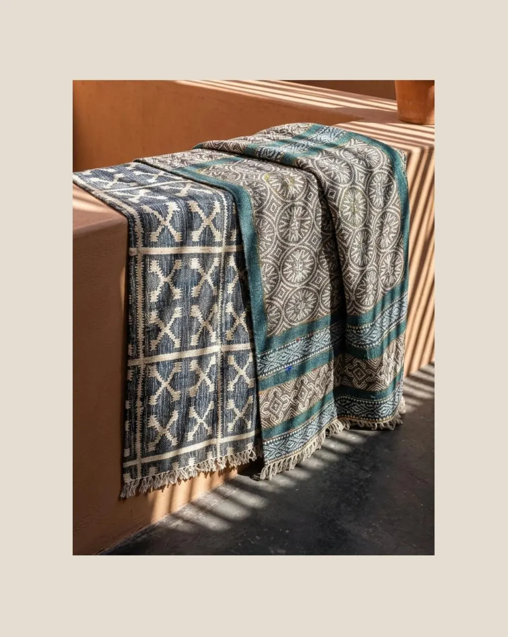 Striped handwoven dhurries in navy, grey and teal draped over a wooden bench in afternoon light