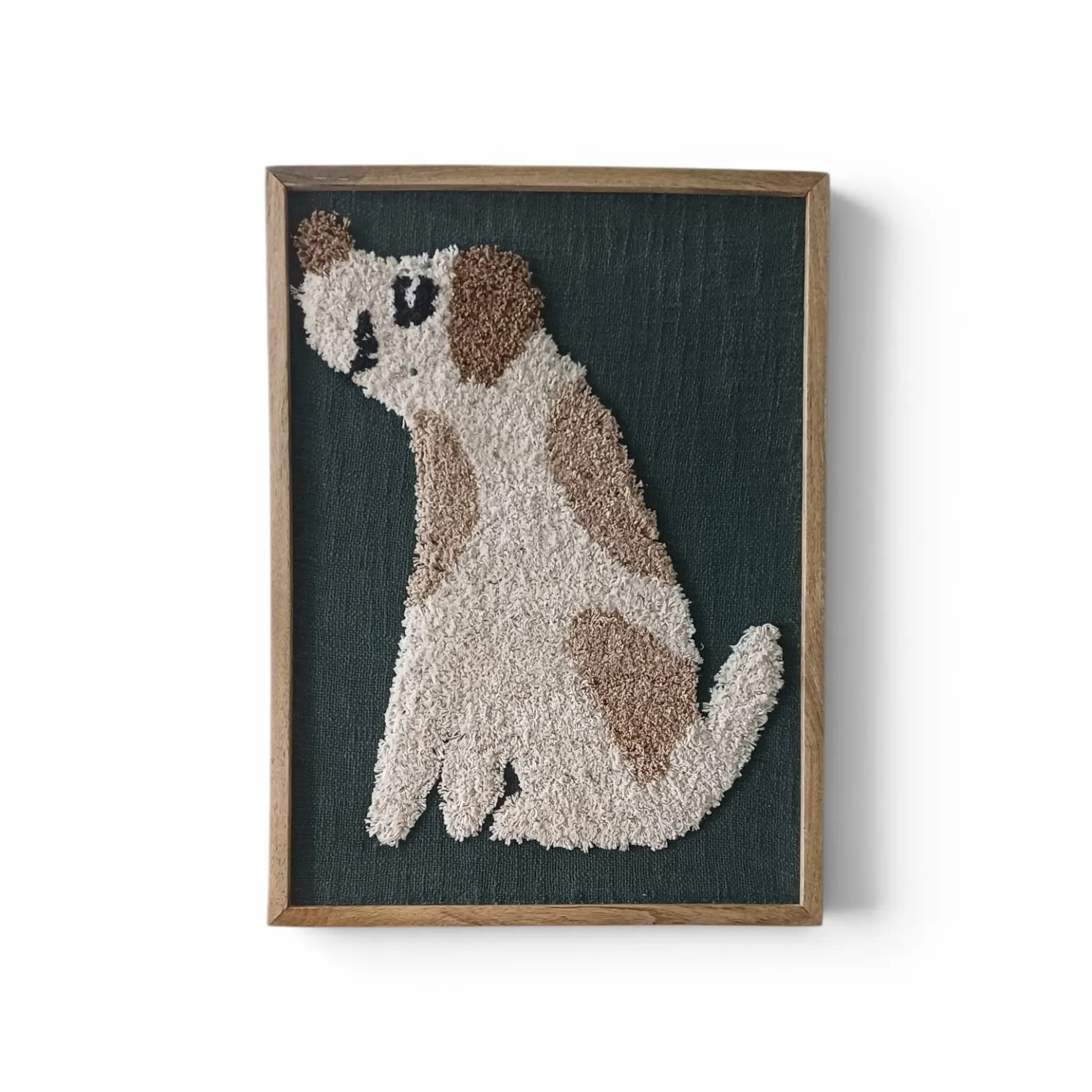 A framed piece of a sitting cream and brown dog on a deep green ground, in a wooden frame