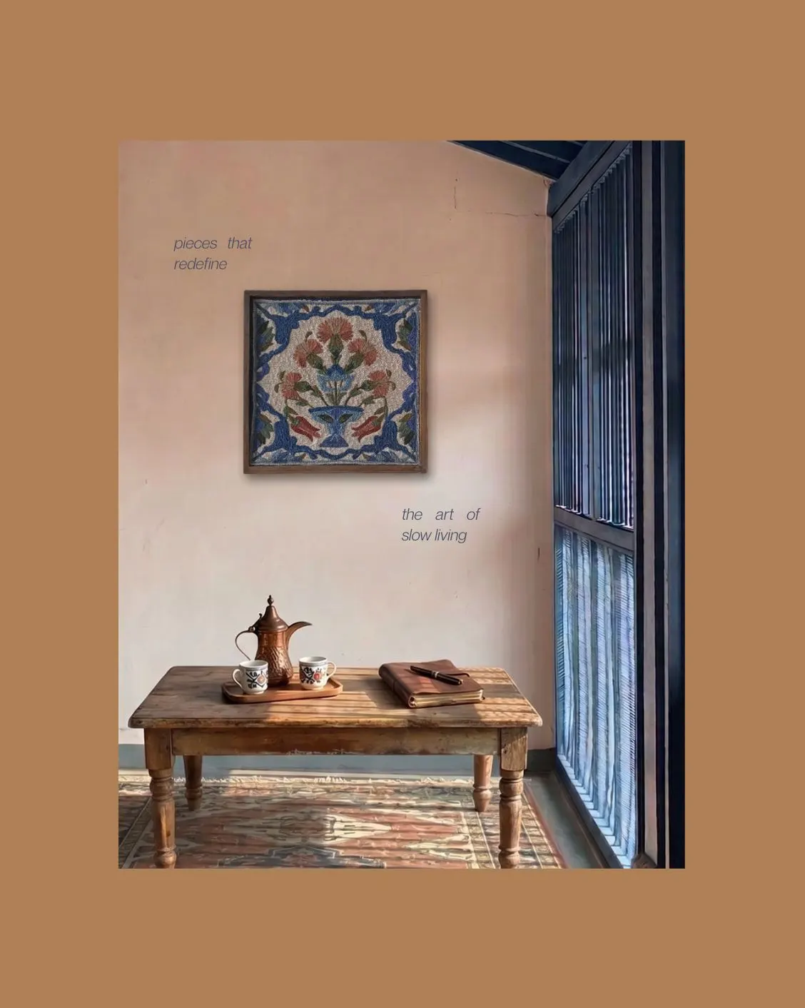 A framed embroidered floral tile on a pink wall above a low wooden table