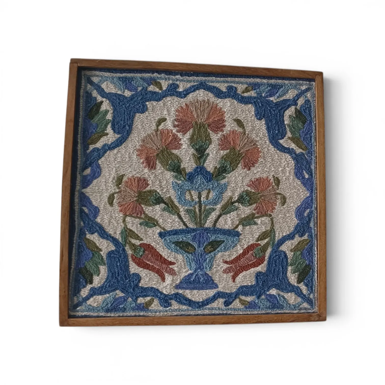 A framed embroidered floral tile with coral flowers in a blue vase, in a wooden frame