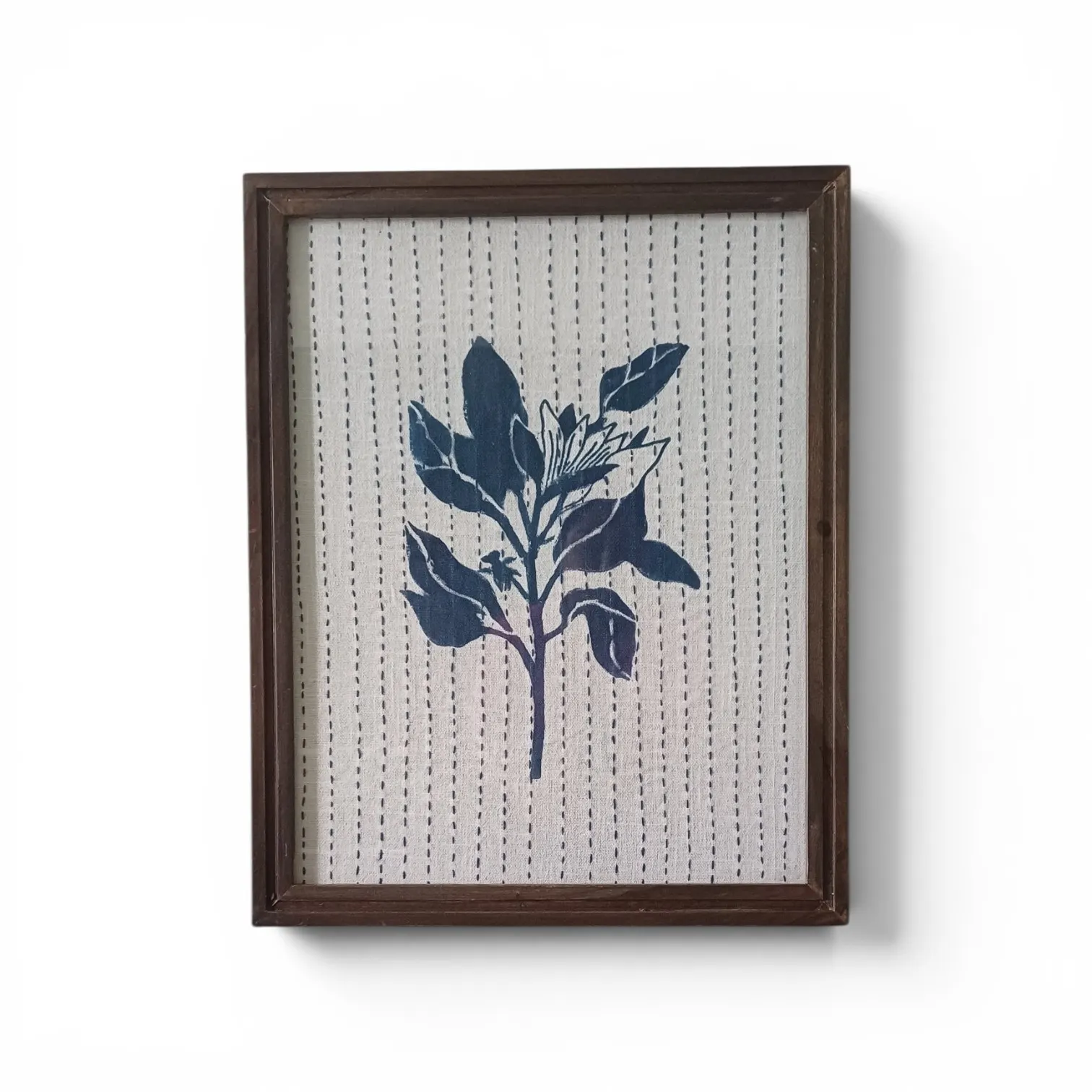A framed indigo leaf motif on white cloth with rows of running stitch, in a dark wooden frame