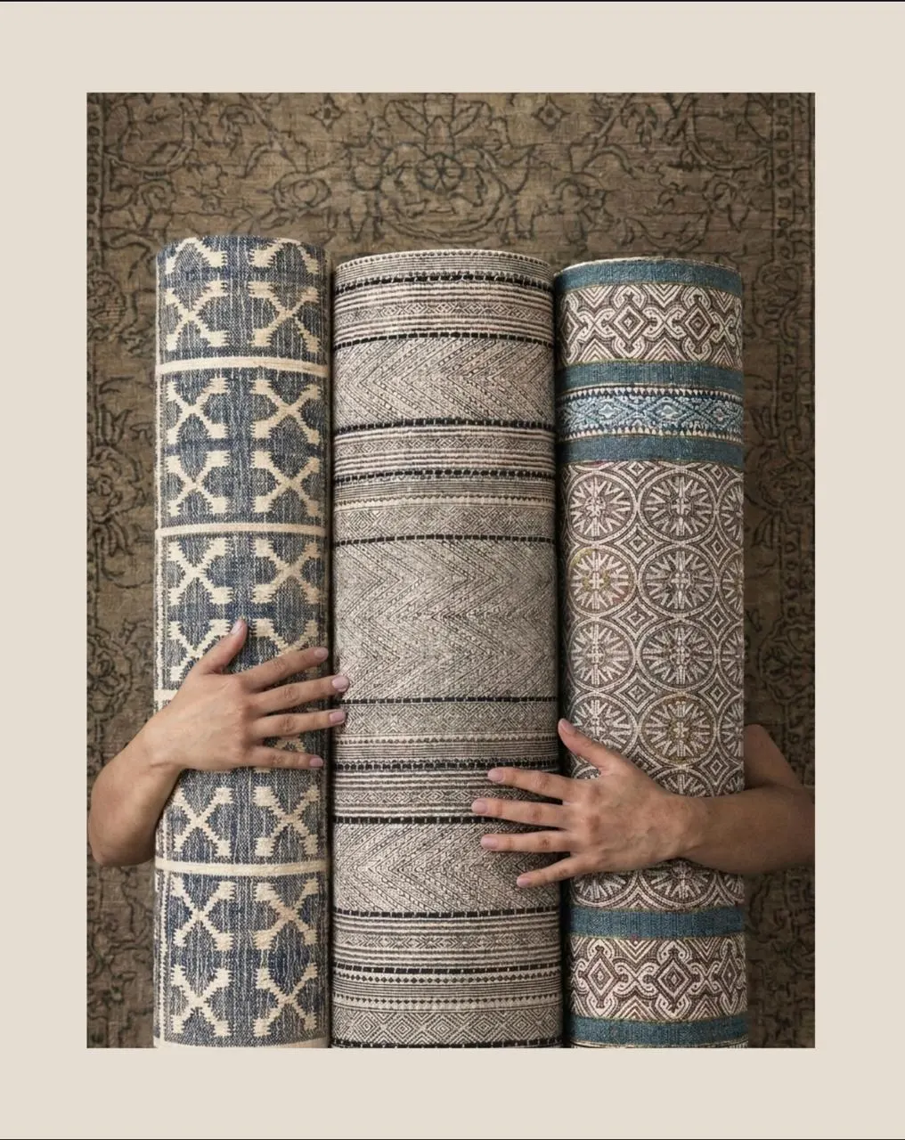 Hands holding three rolled handwoven rugs in blue, grey and natural tones